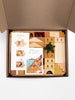 An open cardboard box containing Sabo Concept Italian Ancient City Blocks. The box includes printed paper instructions. A green leaf decoration is on top of the pieces.