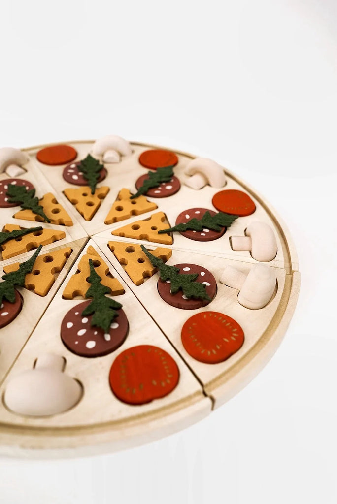 A Sabo Concept Wooden Pizza toy sliced into segments, decorated with pieces resembling cheese, tomatoes, mushrooms, and herbs on a white background.