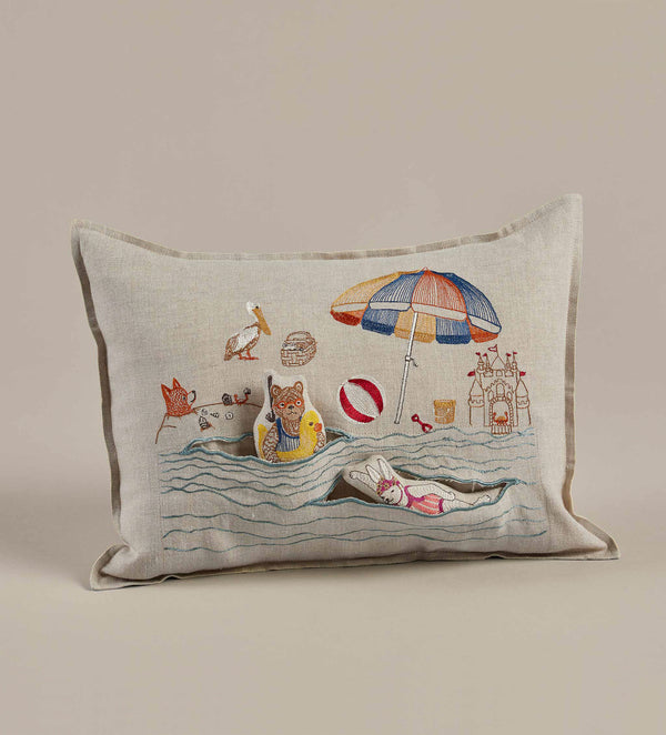 A Coral & Tusk Day at the Beach Pocket Pillow featuring an embroidered beach scene with cats, an umbrella, birds, and a boat on Oeko-Tex certified linen fabric.