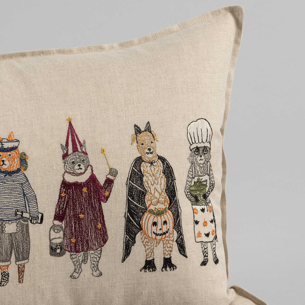 Trick or Treat Pillow featuring embroidered animal characters dressed in various Halloween costumes: a pirate, a wizard, a knight, and a chef, on a beige background.