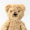 A Slumberkins Honey Bear Kin plush teddy with soft, light brown fur, featuring stitched eyes closed in a peaceful expression and a small, round black nose. The teddy bear is displayed against a plain, light