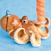 A Octopus Cake Topper with a textured, orange and cream body, holding a pink spiral object. The hand-painted octopus features detailed eyes and suction cups, set against a light blue background.