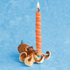 A whimsical, hand painted Octopus Cake Topper shaped like an octopus with a spiraled, lit candle protruding from the top, displayed against a light blue background.