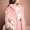 A young girl in a pink fluffy coat carrying a Steiff Unicorn Stuffed Animal, 11 Inches under her arm, posing sideways against a pinkish beige background.