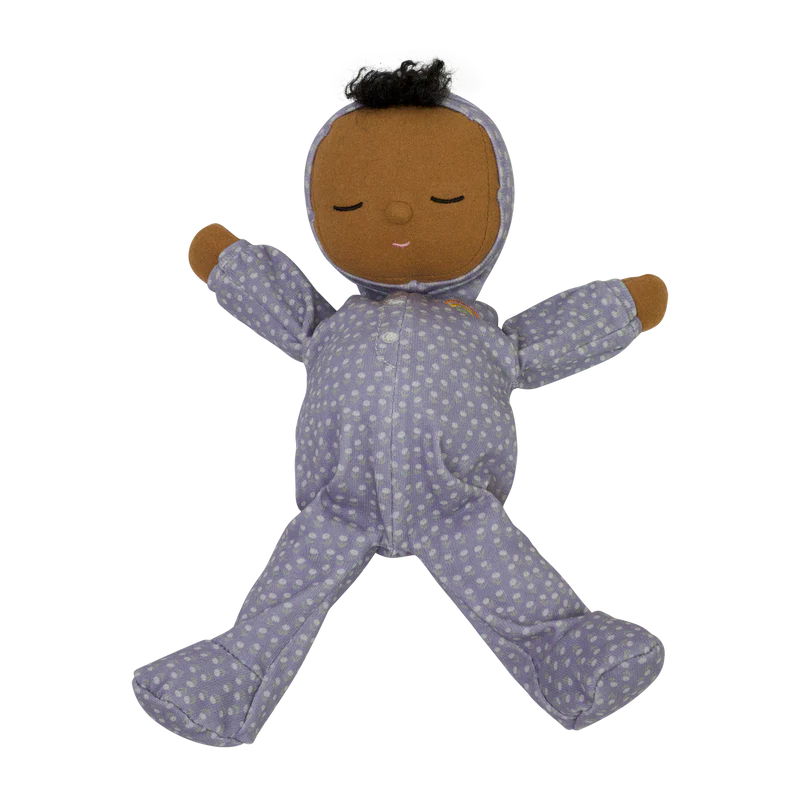 A limited-edition Olli Ella Dozy Dinkums - Squeak baby doll with brown skin and black hair, wearing a purple onesie with an orange zipper, displayed against a black background.