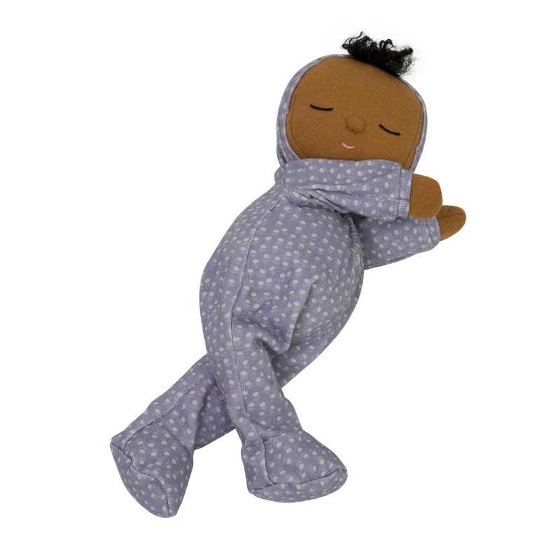 A plush Olli Ella Dozy Dinkums - Squeak from the limited-edition Daydream Collection with dark skin, wrapped in a lavender sleep sack with a polka dot pattern, appearing to be sleeping. The doll has black hair and