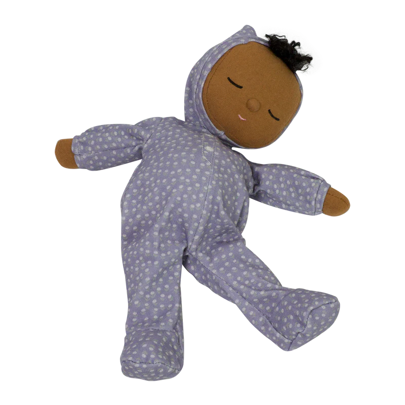 A soft doll from the limited-edition Olli Ella Dozy Dinkums - Squeak Collection with dark skin, dressed in a purple onesie with white polka dots, featuring a hood and a peaceful sleeping expression.