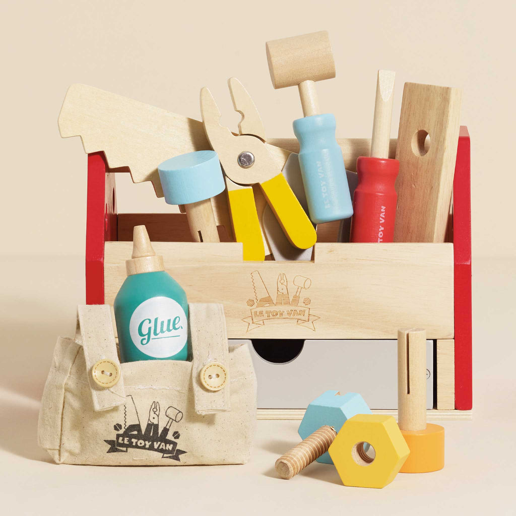 The Tool Box & Wooden Tools set is a perfect early years toy, featuring wooden tools—saw, pliers, hammer, screwdrivers, bolts—plus a cloth bag with a toy glue bottle and large, colorful nuts and bolts in front.