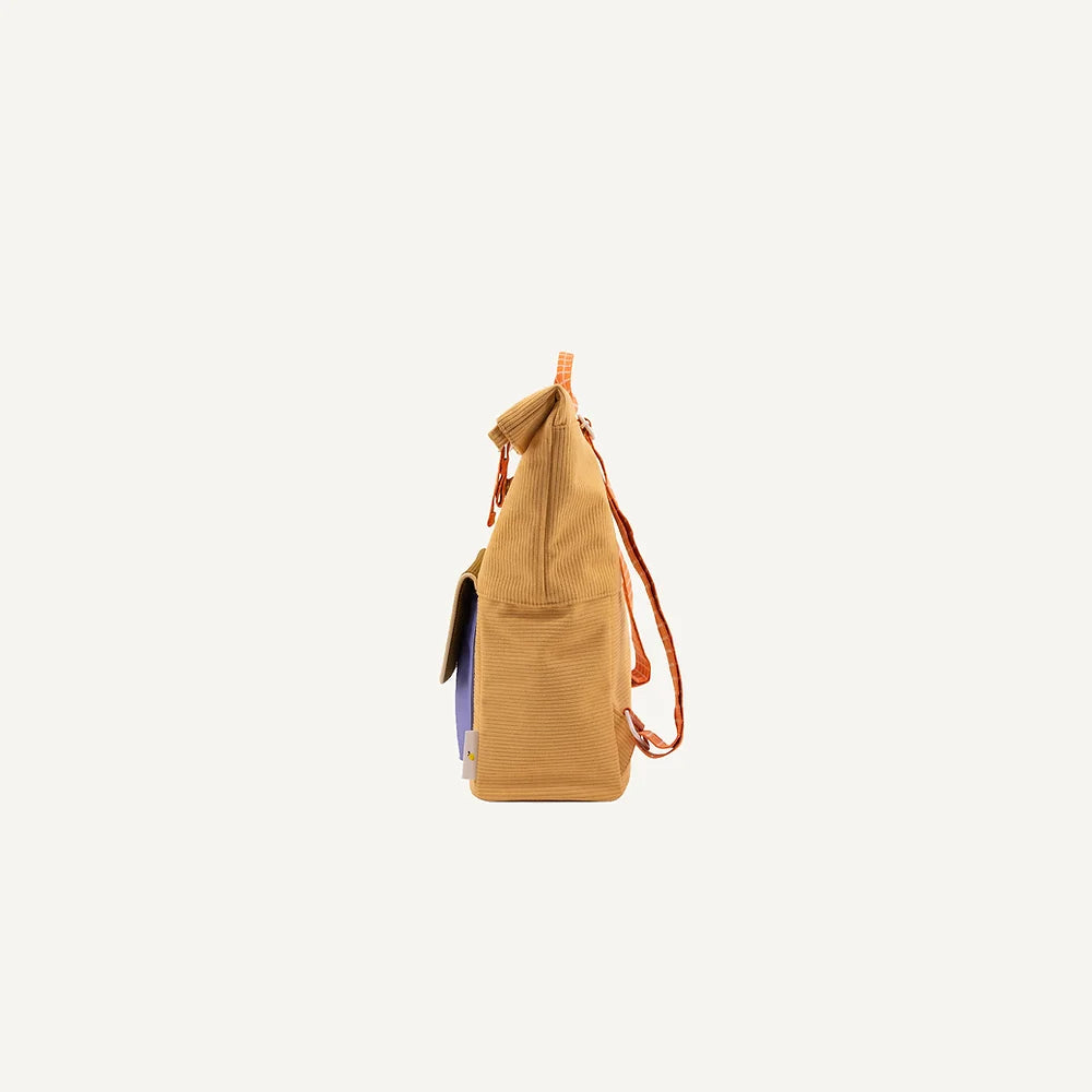 A Corduroy Pear Jam backpack with a brown strap and a trendy tassel on the side, highlighted against a stark white background. The bag is slightly open, showing a glimpse of the blue interior made of.