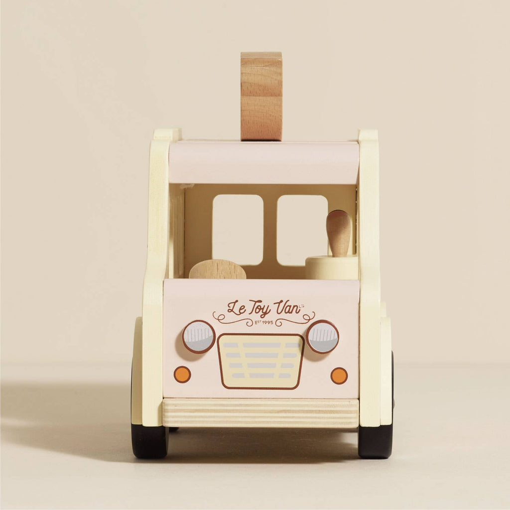 Front view of the Wooden Ice Cream Van, a vintage-style cream and light pink toy with "Le Toy Van" branding, orange headlights, wooden driver, removable roof handle. Ships in one week.