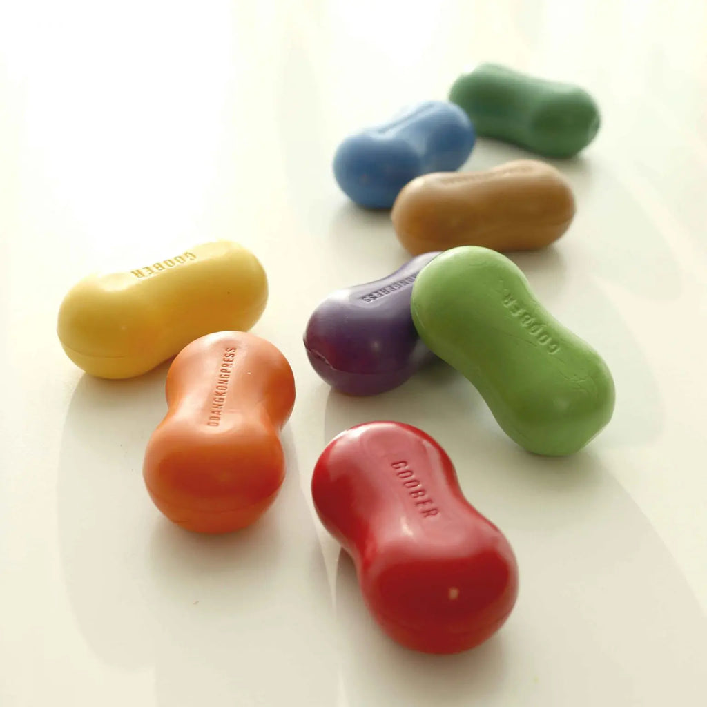 Colorful dumbbell-shaped erasers in various colors (yellow, blue, green, orange, purple, red) arranged on a light surface, with brand names embossed on each Peanut Crayon set.