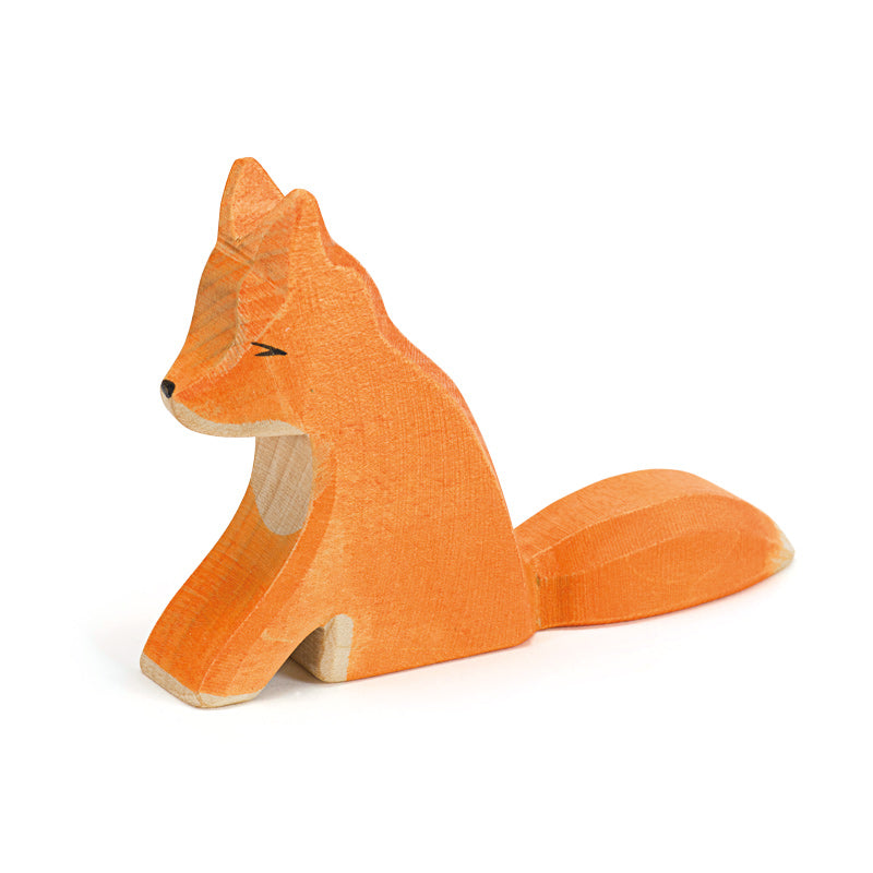Handcrafted wooden toy fox, painted in orange with black accents for eyes and nose. The fox is in a seated position with its tail curled around its side. The texture of the wood grain is visible, giving it a rustic and natural appearance, perfect for imaginative play inspired by Ostheimer Fox - Sitting.