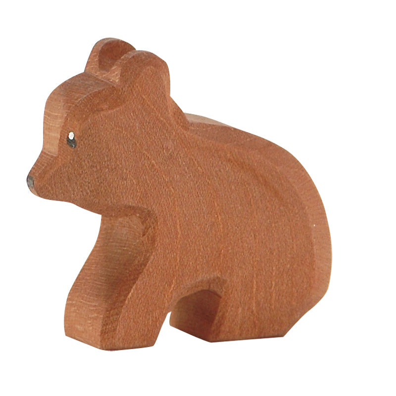 A small, handcrafted Ostheimer Small Bear - Sitting carved out of wood, positioned in profile with a simplistic, stylized form and visible wood grain. The bear has a slight texture and a warm, reddish-brown color.