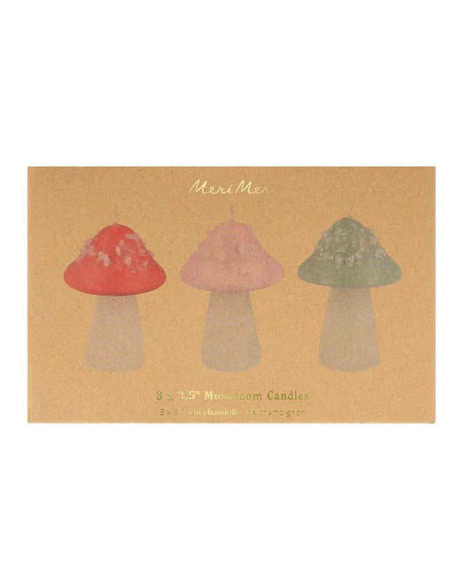 Three Meri Meri Mushroom Candles in red, pink, and green displayed on packaging labeled "meri meri, 3 x 3.5" mushroom candles." The background is beige with.