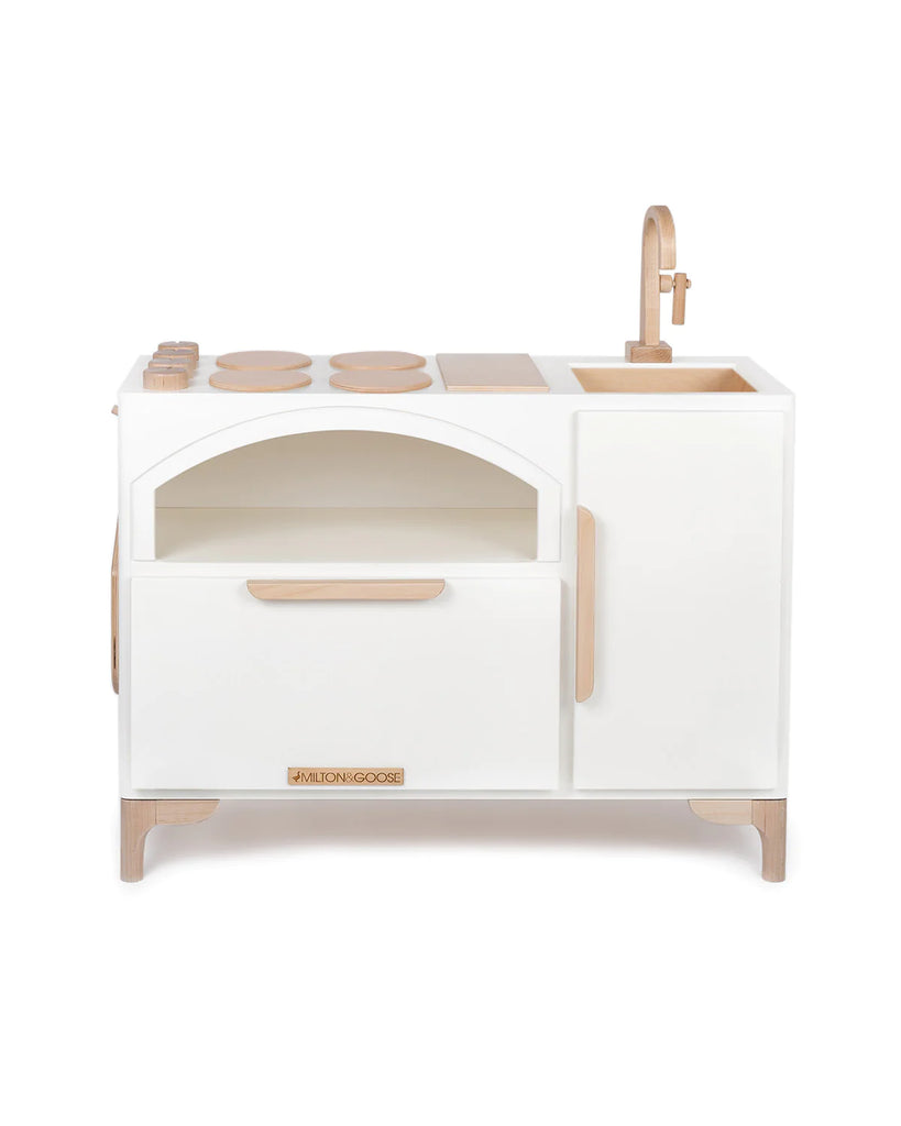 A compact wooden Milton & Goose Play Kitchen With Pizza Oven - Made in USA painted in white and natural wood colors, featuring an oven, stove, and sink with minimalist design elements.