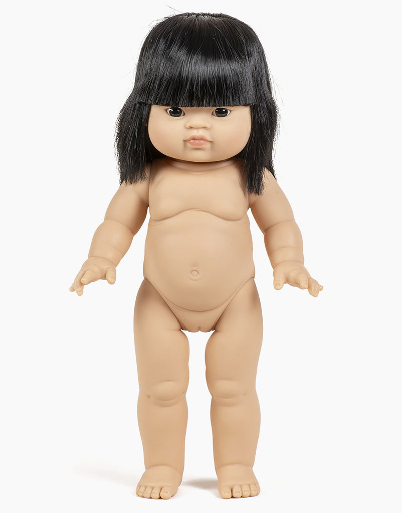 The Minikane Standing Baby Doll (14") - Jade is an anatomically correct doll with straight black hair and bangs, made in Spain. The nude doll stands on a white background with arms slightly out and legs apart. Clothing sold separately.