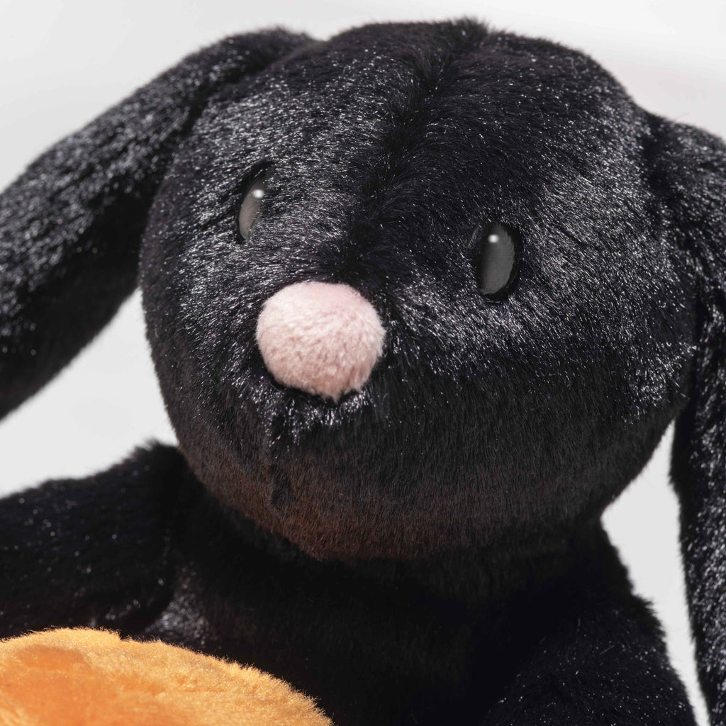Close-up of Steiff Mr. Spice Hoppie Rabbit, a black Halloween plush with floppy ears, shiny black eyes, a soft pink nose, and velvety fur. A light brown object appears at the bottom of the image.
