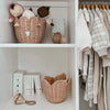 A neatly organized nursery closet featuring two shelves: the top shelf displays a Olli Ella Rattan Lily Basket Set with a sleeping doll and a teddy bear, while the second shelf houses baby clothes and a stack of books.