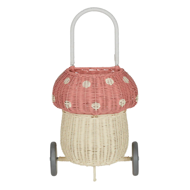 The Olli Ella Rattan Mushroom Luggy - Pink is a woodland-inspired, two-wheeled basket shaped like a mushroom, with a beige base, pink spotted cap, hand-woven rattan body, and a curved white handle on top.