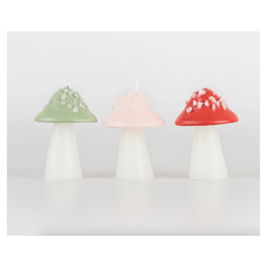 Three Meri Meri Mushroom Candles in green, pink, and red, each with white stems and decorative accents on their colored caps, displayed against a light grey background.