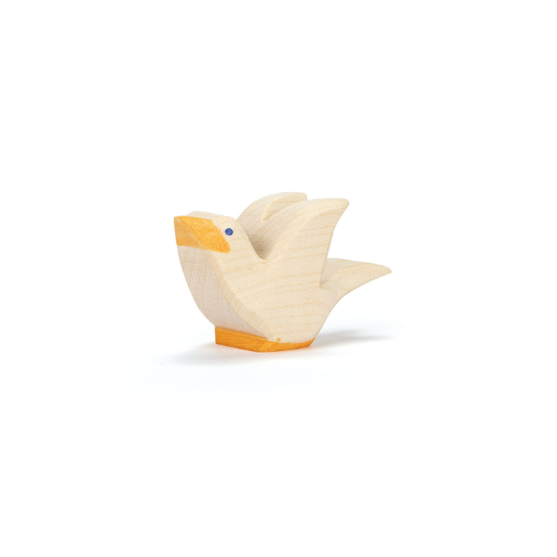 The Ostheimer Flying Pigeon is a small, light-colored wooden bird figurine with a yellow beak and underside, featuring a simple painted eye. Handcrafted from non-toxic materials, it stands on a white background as an example of quality toy design.