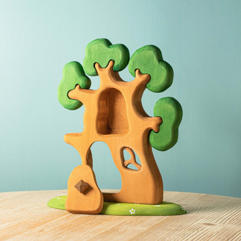 The Bumbu Handmade Wooden Ancient Oak Tree with Owl Set features a sustainable oak treehouse on a green base, with detailed foliage, a hollow trunk and small door, white flower accents, and an owl—perfect for imaginative play.