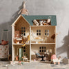 A detailed wooden Maileg Dollhouse with open back showing rooms furnished with miniature Maileg Furniture and decor. Toys scattered around the house on a textured grey background.