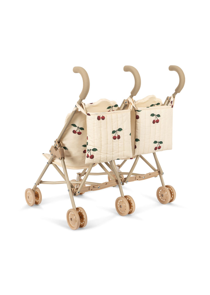 The Konges Sloejd Twin Doll Stroller - Cherry features a beige frame, tan wheels, curved handles, and quilted cherry-patterned seats, allowing two dolls to ride side by side in charming style.
