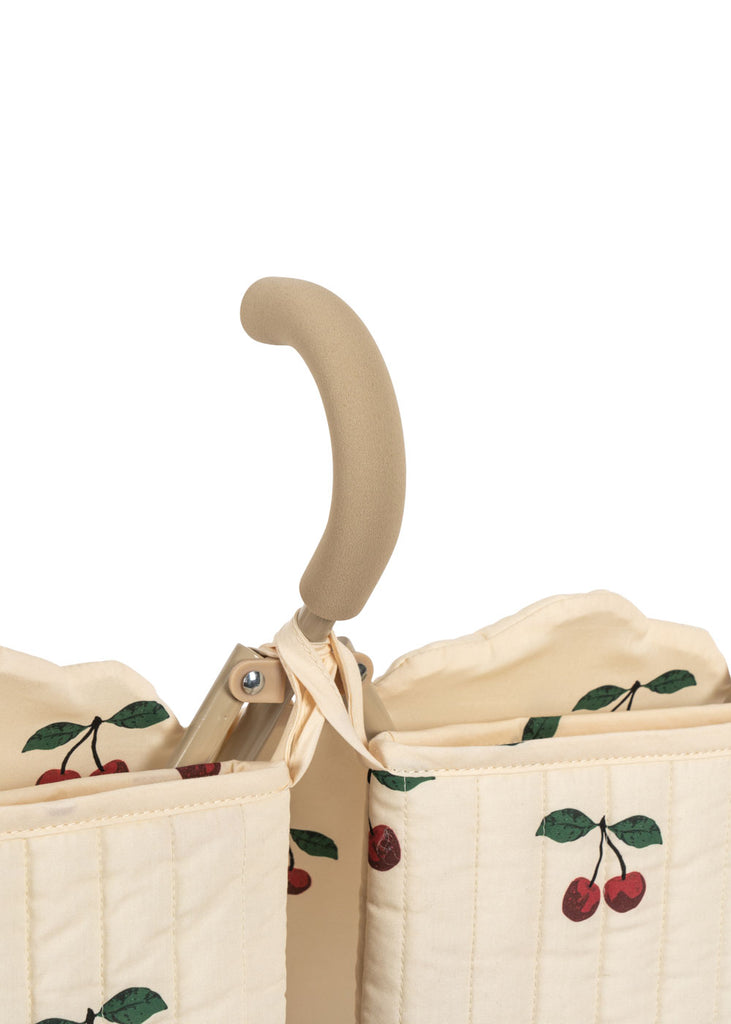 Close-up of a beige, quilted fabric bag with cherry print and padded handle, designed for the Konges Sloejd Twin Doll Stroller - Cherry. The partially open bag reveals two soft-edged compartments and metal hardware on the handle.