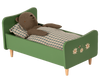 A Teddy Dad - Dusty Green tucked into a child's wooden bed with green frames, handpainted details, and floral decoration. The bear is lying on a checkered blanket.