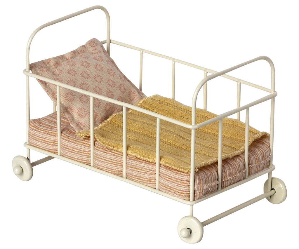 A Maileg Micro Cot with a metal frame and wheels, equipped with a pink floral mattress and a yellow knitted blanket.