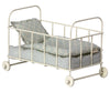 A Maileg Micro Cot with rolling wheels, featuring a floral-patterned mattress and pillow in shades of blue and white.