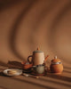 A serene still life setup of a Handmade Wooden Tea Set - Herbal with a teapot, cups, sugarcube bowl, and plates on a table, all cast in warm, soft lighting with shadow patterns on the.