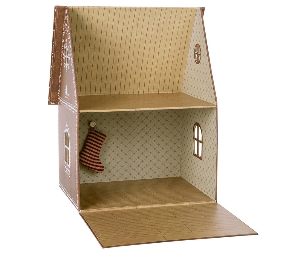 A small, open-front Maileg Cardboard Gingerbread House made of cardboard, featuring two floors with decorative wallpaper in a gingerbread style. The lower floor has a blue pattern, while the upper floor has a striped design. Perfect for micro Maileg friends, it includes a miniature red and white stocking hanging inside.