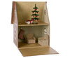 A miniature, whimsical cardboard house reminiscent of a Maileg Cardboard Gingerbread House with two floors. The upper floor features a Christmas tree adorned with ornaments and presents underneath. The lower floor contains two armchairs, a small table, and a striped stocking hanging on the wall—perfect for micro Maileg friends to enjoy holiday surprises.
