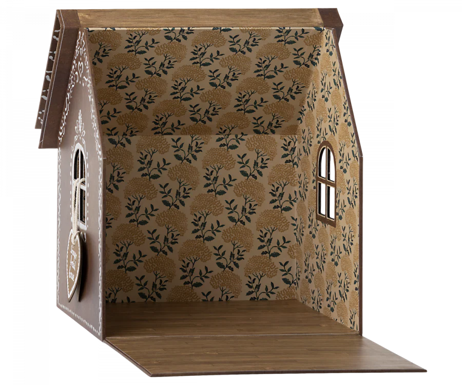 A small, open-front Maileg Cardboard Gingerbread House with intricate wallpaper featuring a gold floral pattern on a white background. The walls have wooden window frames, and the ceiling has a brown wooden beam with decorative edges. Perfect for housing your micro Maileg friends, the floor is made of wooden planks.