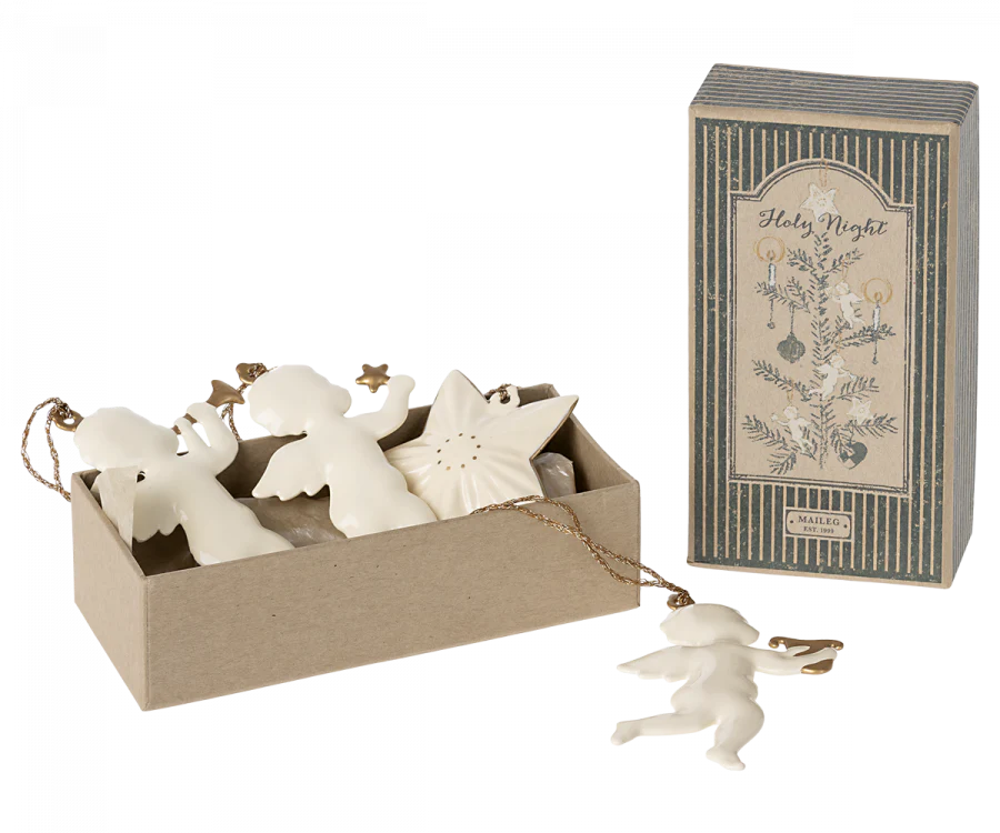 A decorative gift box containing the Maileg Holy Night Ornament Set, which includes white angel and star ornaments, rests next to its matching packaging labeled "Holy Night." These charming decorations are designed with gold hanging strings.