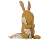 A Maileg Lullaby Friends - Bunny (Plays Music) made of yellow fabric sits upright, holding a white blanket adorned with multicolored polka dots. The lullaby stuffed animal features long, floppy ears with a textured inner lining and simple stitched facial features—a perfect gift for babies.
