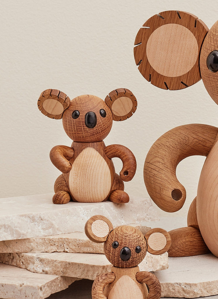 Three Spring Copenhagen Matilda koala bear figurines of different sizes, crafted with visible wood grains and smooth finish, positioned on a stone surface against a light beige background.