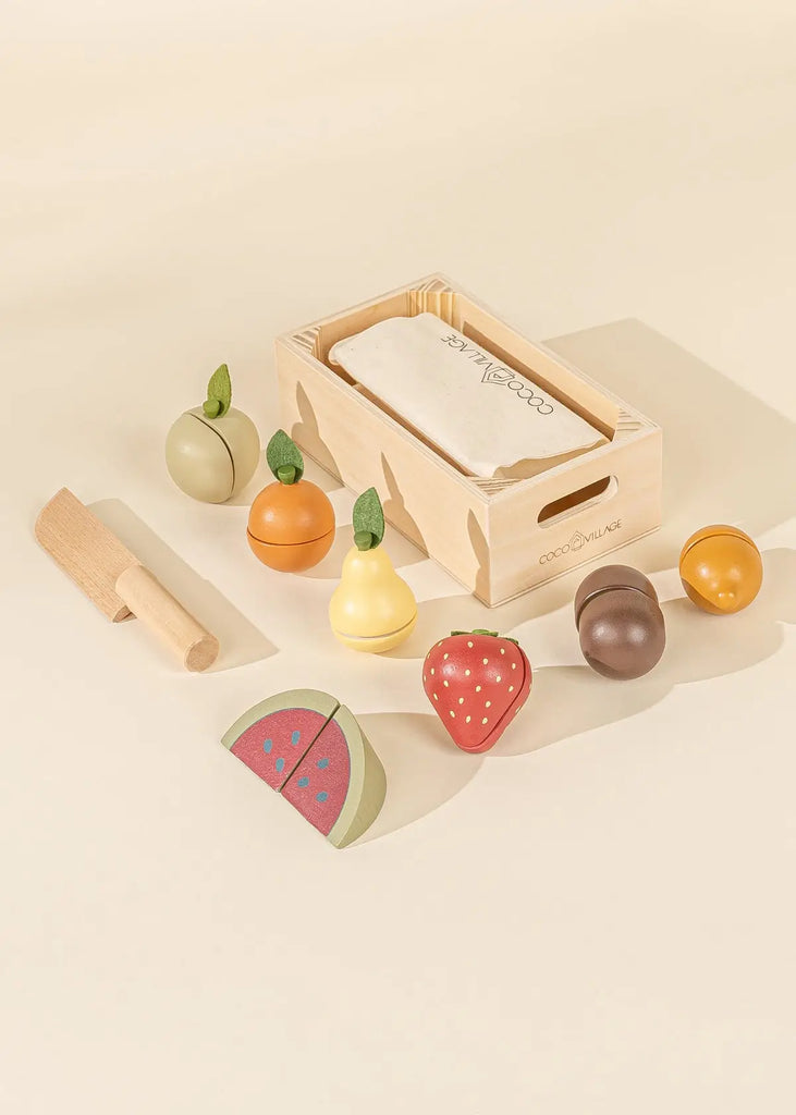 Natural color wooden crate with folded beige canvas bag in it. Wooden fruits lined up. Green wooden apple, wooden orange, wooden yellow pear, wooden red strawberry, wooden brown kiwi, wooden watermelon slice, wooden orange mandarin. One natural color wooden pretend play knife.