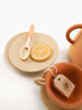 Handmade Wooden Tea Set - Herbal featuring a plate with a lemon slice design cookie, a spoon and a teacup, accompanied by a teapot, all painted with non-toxic paint in warm earth.