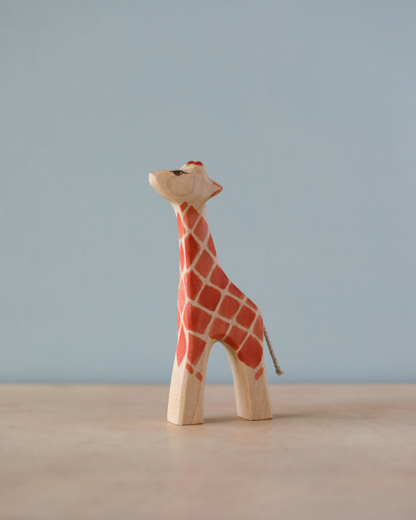 A Handmade Holzwald Giraffe - Small, crafted from high-quality materials, features a hand-painted red and white pattern and stands against a simple blue background. The giraffe appears cheerful, with a tiny tail.