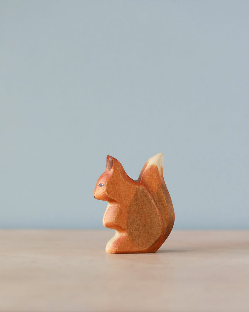 A handmade Holzwald Squirrel stands on a plain surface against a soft blue background, elegantly capturing simple artistic detail and natural wood grain.