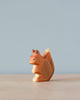 A Handmade Holzwald Squirrel figurine set against a soft blue background, beautifully carved showing detailed textures, positioned in a sideways stance on a flat surface.