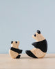 Two Handmade Holzwald Baby Panda wooden toys on a table, facing each other against a soft blue background. The larger panda is sitting while the smaller one appears to be looking up at it.