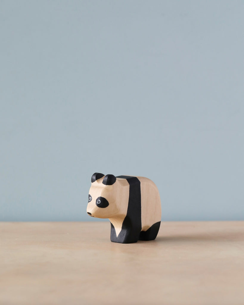 A Handmade Holzwald Baby Panda wooden toy with black and white patterns, positioned on a plain surface against a light blue background.