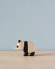A handmade Holzwald Baby Panda, painted in natural wood and black colors, standing against a pale blue background.