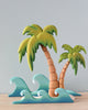 Two Set of Handmade Wooden Palm Trees & Waves with stylized green leaves and textured trunks, set against waves crafted from layers of blue painted wood, on a plain background.