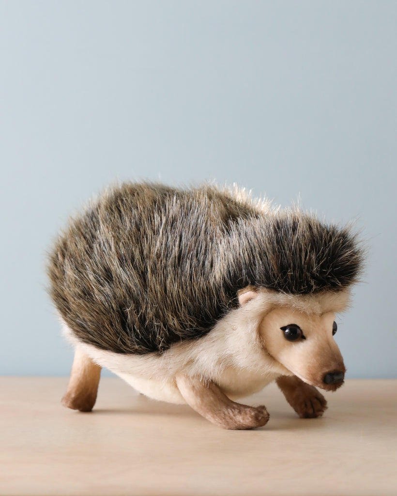 A realistic Hedgehog Stuffed Animal on a wooden surface against a light blue background. The hedgehog is detailed, capturing its spines, small eyes, and tiny paws in a natural color.