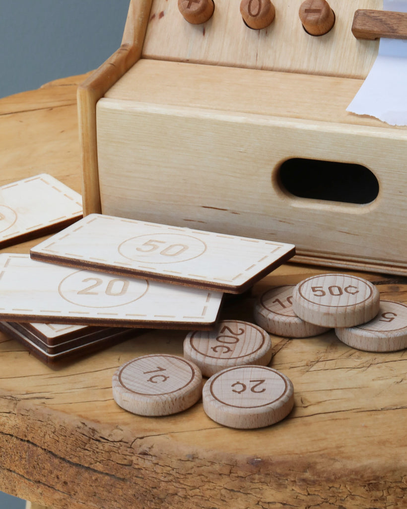 Wooden Cash Register featuring number tiles and circular number coins scattered on a table, partially assembled in a wooden box with compartments, all made from sustainably sourced wood.